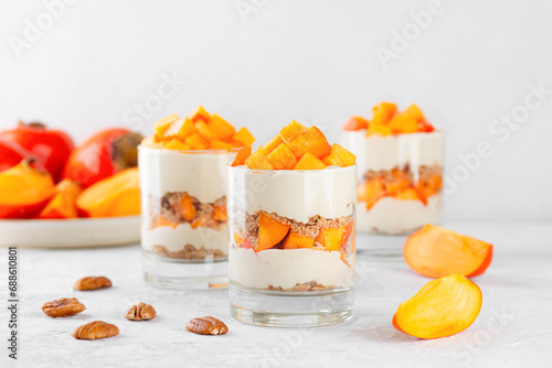 Parfait in a glasses with persimmon, pecan, whipped cream and biscuit. Healthy food, vegan, sugar, gluten and lactose free.