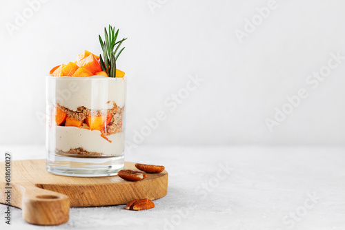 Dessert in a glass with persimmon, rosemary, pecan, whipped cream and biscuit. Healthy food, vegan, sugar, gluten and lactose free.