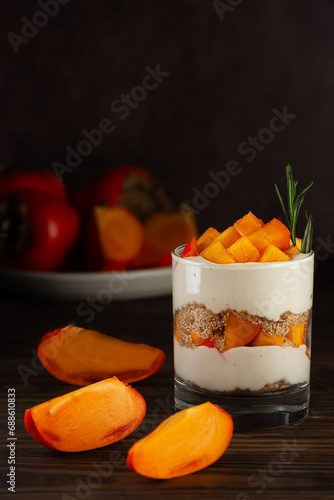 Trifle in a glass with persimmon, rosemary, pecan, whipped cream and biscuit on a brown. Healthy food, vegan, sugar, gluten and lactose free.