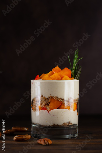 Dessert in a glass with persimmon, rosemary, pecan, whipped cream and biscuit on a brown. Healthy food, vegan, sugar, gluten and lactose free.