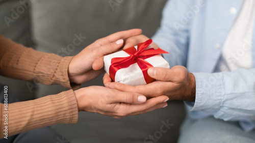 Closeup of young couple's hands holding wrapped gift box indoors