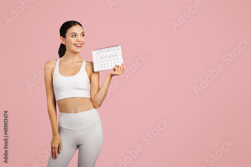 Young european slim woman in sportswear holding calendar, isolated on pink studio background, free space photo