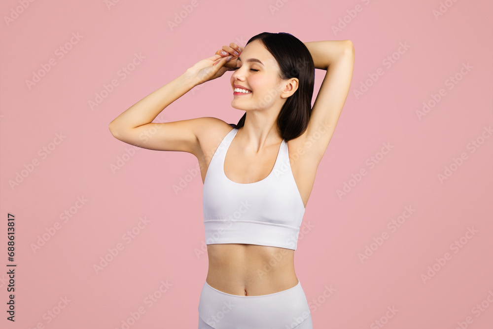 Slim young lady athlete in sportswear enjoy workout, stretching hands on pink studio background Slim young lady athlete in sportswear enjoy workout, stretching hands on pink studio background