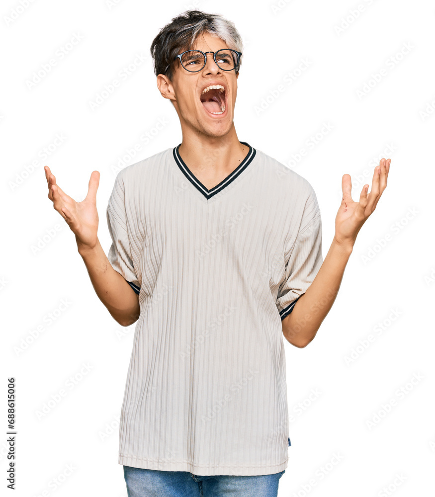 Young hispanic man wearing casual clothes and glasses crazy and mad shouting and yelling with aggressive expression and arms raised. frustration concept. Young hispanic man wearing casual clothes and glasses crazy and mad shouting and yelling with aggressive expression and arms raised. frustration concept.