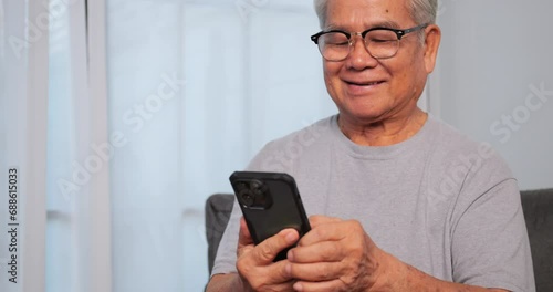 Asian old man using smart phone while sitting on sofa at home. photo