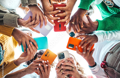 Group of young people using smart mobile phone device outside - Trendy technology concept with guys and girls playing video games app on smartphone - Bright colorful filter photo