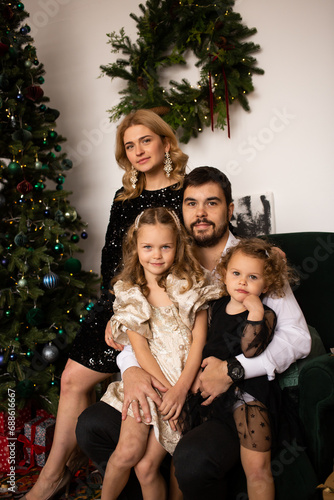 father, mother and girls sister smile on a background of Christmas trees in the interior of the house