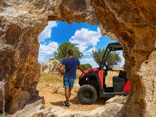 Tourist in Cyprus. Man travels around city of Paphos. Guy next to tourist car. Male tourist admires nature. Traveling around Cyprus. Man near rock with arch. Traveler surveys landscape photo