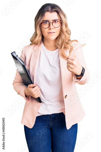 Young caucasian woman wearing business clothes and glasses holding binder annoyed and frustrated shouting with anger, yelling crazy with anger and hand raised