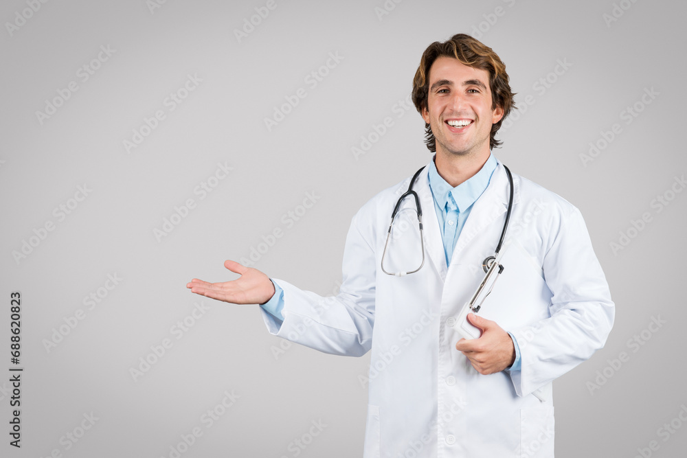 Smiling male doctor in lab coat gesturing with hand on grey background Smiling male doctor in lab coat gesturing with hand on grey background