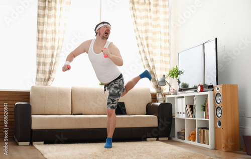 Young handsome man in shorts and vest holds pink dumbbells in hand. Watch tv lessons single combats is practicing receptions of sensei one home fitness indoor training independent education remotely photo