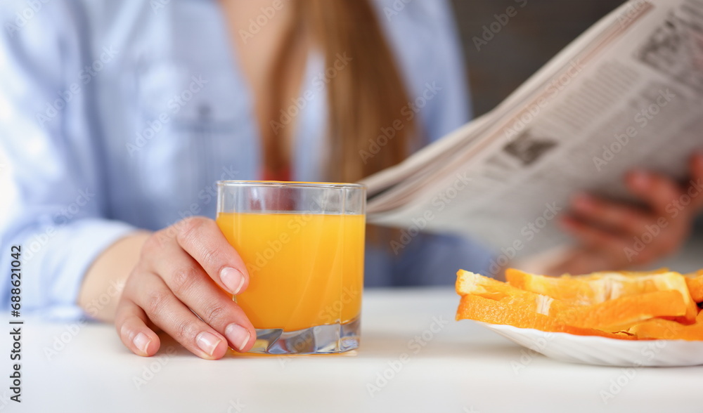 Beautiful smiling brunette woman hold in arms glass of orange juice at kitchen table and newspaper closeup. Weight loss beauty fit concept Beautiful smiling brunette woman hold in arms glass of orange juice at kitchen table and newspaper closeup. Weight loss beauty fit concept