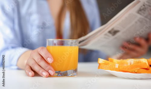 Beautiful smiling brunette woman hold in arms glass of orange juice at kitchen table and newspaper closeup. Weight loss beauty fit concept
