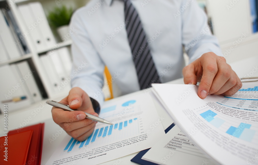 Male hands hold documents with financial statistics at office workspace closeup. White collar check money papers stock exchange market internal Revenue Service inspector earning list concept Male hands hold documents with financial statistics at office workspace closeup. White collar check money papers stock exchange market internal Revenue Service inspector earning list concept