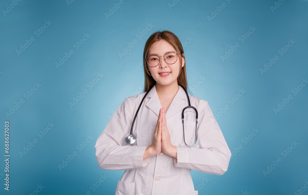 Young asian doctor wear medical uniform lab coat and stethoscope on blue background. Smiling female doctor with pay respect gesture Thai culture Young asian doctor wear medical uniform lab coat and stethoscope on blue background. Smiling female doctor with pay respect gesture Thai culture