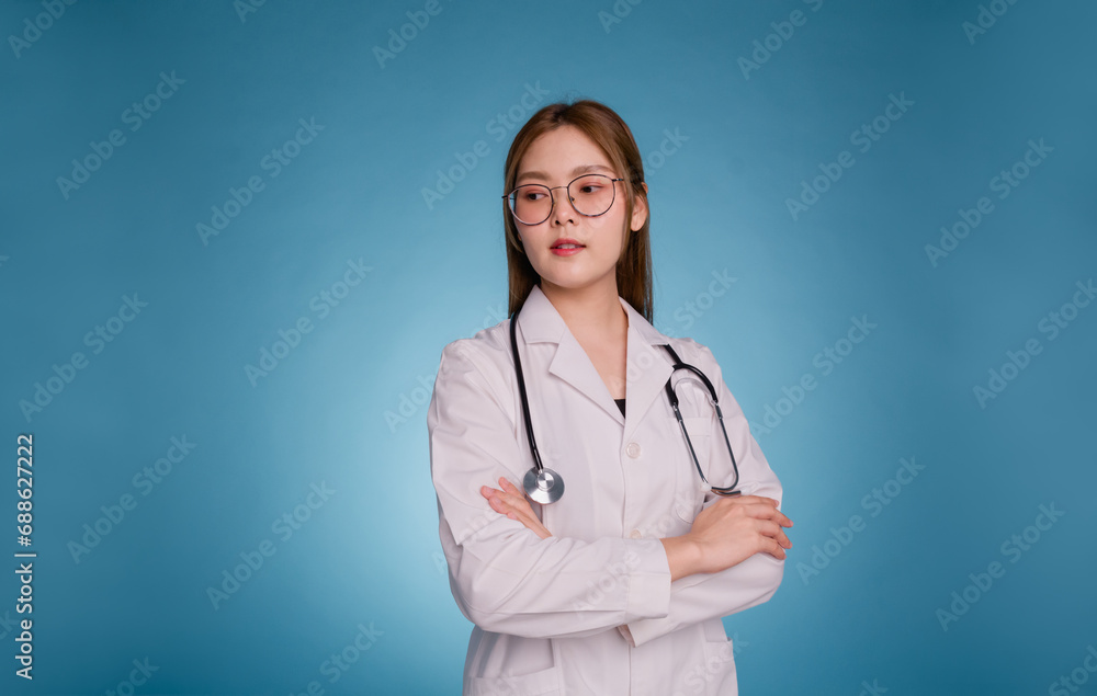 Portrait of smiling female doctor with arms crossed. Young asian doctor wear medical uniform lab coat and stethoscope isolated over blue color background. Healthcare and medical staff concept.. Portrait of smiling female doctor with arms crossed. Young asian doctor wear medical uniform lab coat and stethoscope isolated over blue color background. Healthcare and medical staff concept..