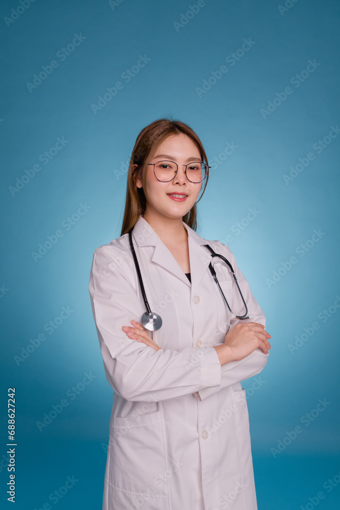 Portrait of smiling female doctor with arms crossed. Young asian doctor wear medical uniform lab coat and stethoscope isolated over blue color background. Healthcare and medical staff concept.. Portrait of smiling female doctor with arms crossed. Young asian doctor wear medical uniform lab coat and stethoscope isolated over blue color background. Healthcare and medical staff concept..