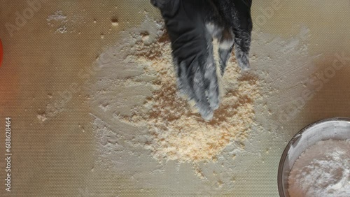 Mixing flour with powdered sugar and egg yolks by hand to obtain a shortbread dough. The process of making dough on a silicone mat