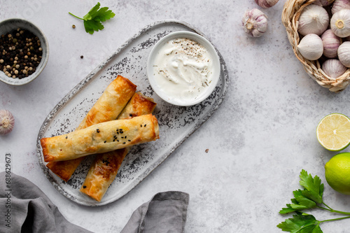 Turkish Cigara Börek (Sigara böreği) or Cigarette Pastry with Spinach and Feta Cheese with yogurt dip. Finger food. Spring rolls. Top view photo