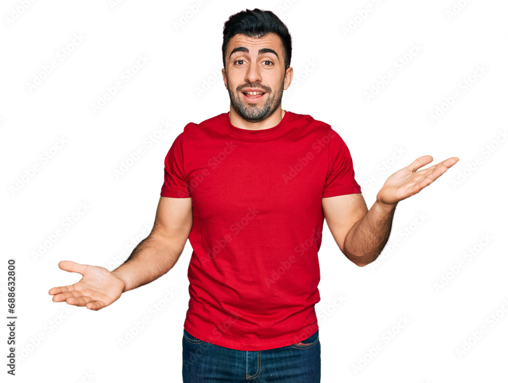 Hispanic man with beard wearing casual red t shirt clueless and confused expression with arms and hands raised. doubt concept. Hispanic man with beard wearing casual red t shirt clueless and confused expression with arms and hands raised. doubt concept.