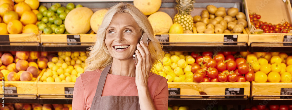happy female seller smiling and talking by phone with fruits and vegetables on backdrop, banner