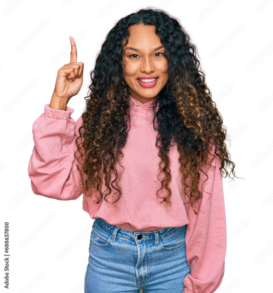Young hispanic woman with curly hair wearing casual sweatshirt pointing finger up with successful idea. exited and happy. number one. Young hispanic woman with curly hair wearing casual sweatshirt pointing finger up with successful idea. exited and happy. number one.