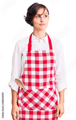 Beautiful young woman with short hair wearing professional cook apron smiling looking to the side and staring away thinking.