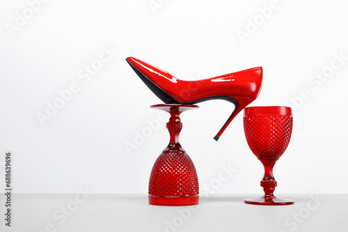 Red wine glasses and a red women's high heel shoe on a white table and background. Balancing composition. Copy space photo
