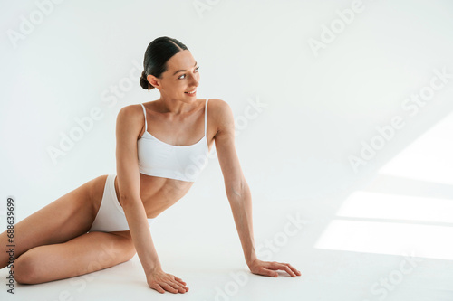 Posing for the camera. Woman in white underwear with slim body type against white background