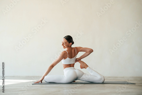 Stretching the legs. Fitness woman is indoors in white clothes