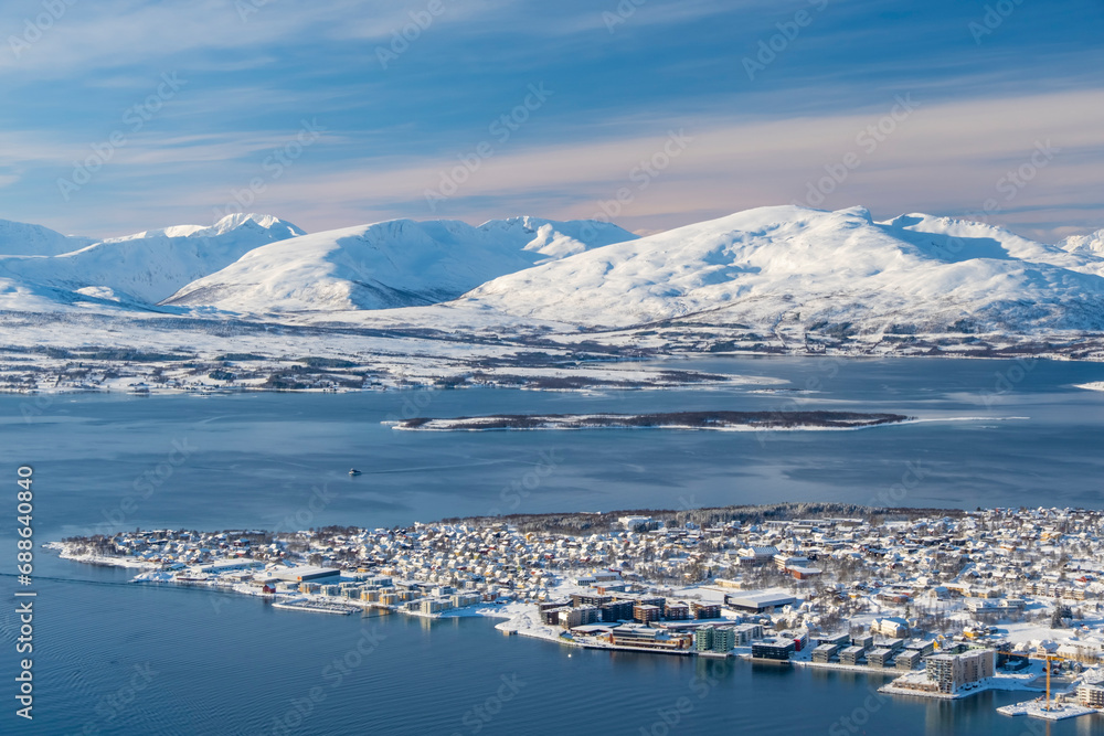 Panorama of norwegian city of Tromso in the winter. Snowy roofs, embankment near the port and fishing ships, Sunny winter day.