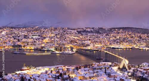 Panorama of Norwegian city of Tromso in the winter. Snowy roofs, bridge, embankment near the port and fishing ships. Evening lights photo