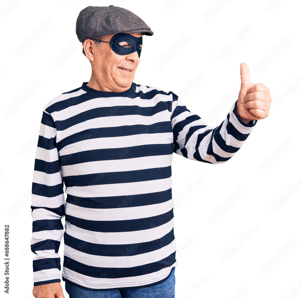 Senior handsome man wearing burglar mask and t-shirt looking proud, smiling doing thumbs up gesture to the side Senior handsome man wearing burglar mask and t-shirt looking proud, smiling doing thumbs up gesture to the side