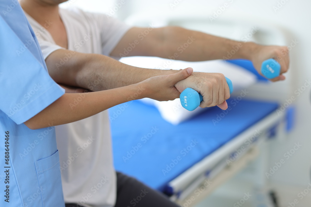 Nurse in an examination room at a hospital is doing physiotherapy for a male patient's arm with dumbbells lifting up and down. Nurse in an examination room at a hospital is doing physiotherapy for a male patient's arm with dumbbells lifting up and down.