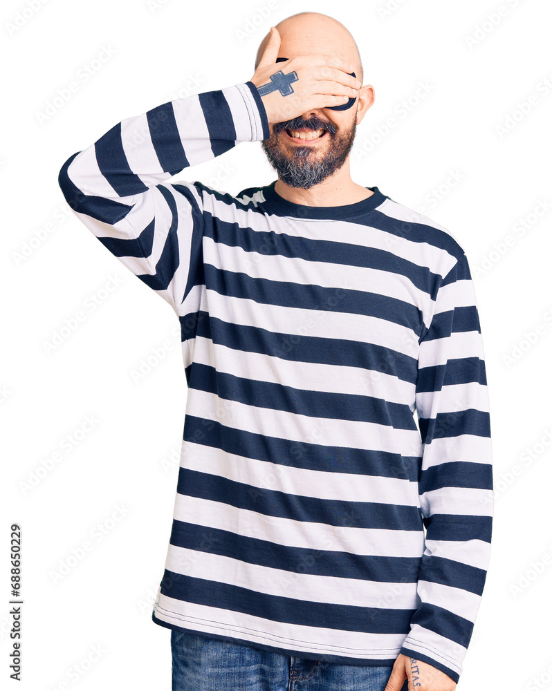 Young handsome man wearing burglar mask smiling and laughing with hand on face covering eyes for surprise. blind concept. Young handsome man wearing burglar mask smiling and laughing with hand on face covering eyes for surprise. blind concept.