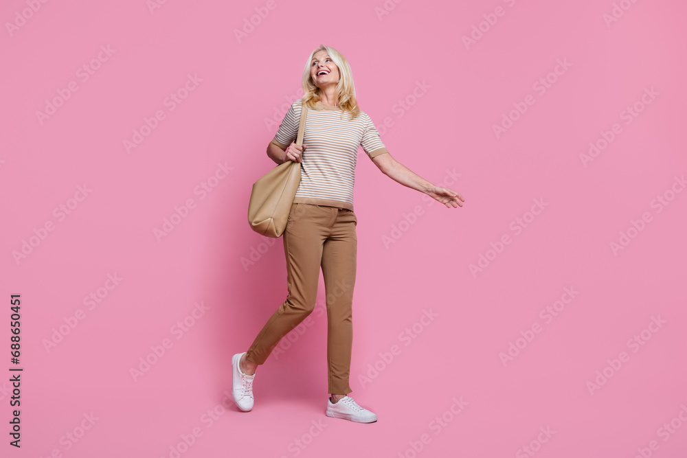 Full size photo of cheerful gorgeous person hold purse walk look empty space isolated on pink color background Full size photo of cheerful gorgeous person hold purse walk look empty space isolated on pink color background