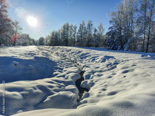 White winter landscape with big ditch, trees, bushes and vegetation covered with snow after a heavy snowfall on a sunny day. Snowy winter fairytale © KristineRada