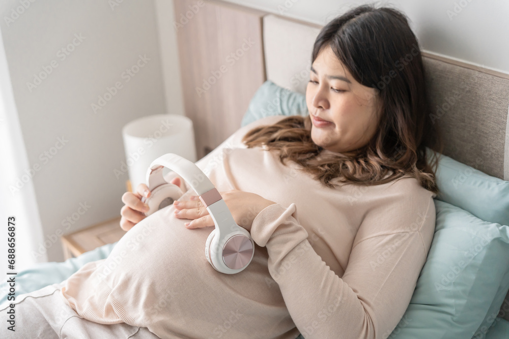 Pregnant asian woman holding headphone on belly playing music to her baby in stomach relaxing pregnancy Mental health concept Pregnant asian woman holding headphone on belly playing music to her baby in stomach relaxing pregnancy Mental health concept