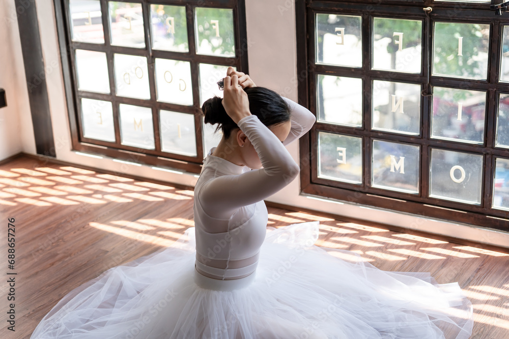 Naklejka premium Asian girl ballet dancer preparing fixing her hair into a bun during ballet class. ballerina adjusting her hair