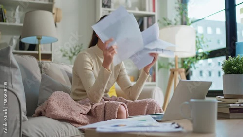 Woman going through bills, looking worried. Young adult asian woman female reading her bill papers and getting headache from stress Young asian woman at home paying online bills photo