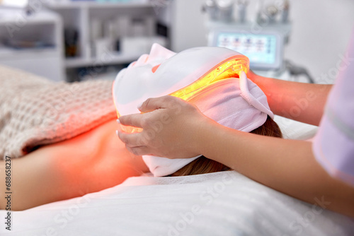 woman receiving led light anti-aging mask treatment from beautician in beauty salon photo