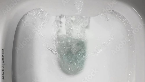 Close-up of water flowing into a white urinal with foamy bubbles, depicting hygiene and restroom facilities photo