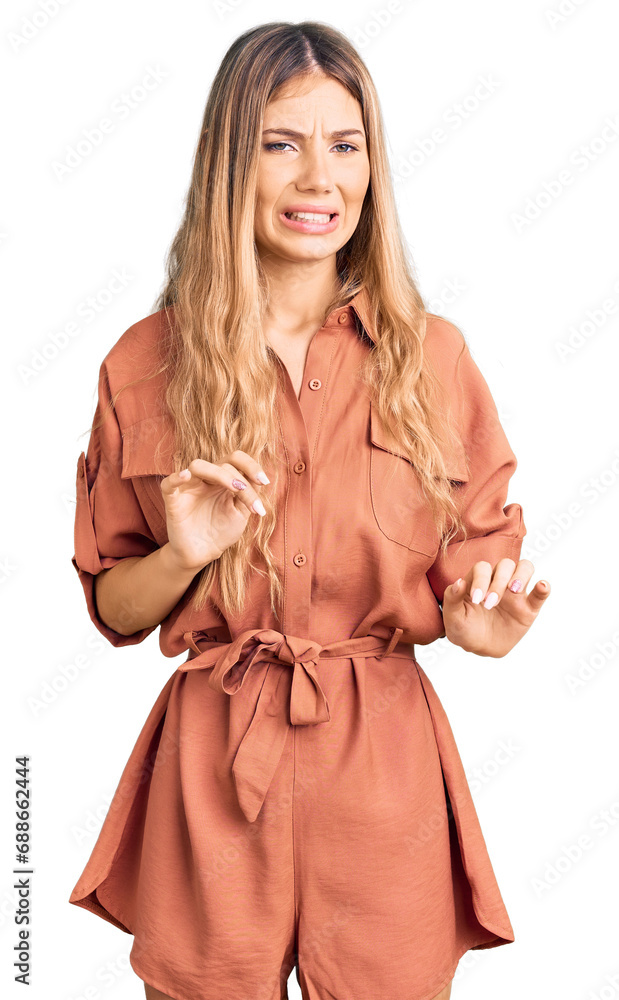 Beautiful caucasian woman with blonde hair wearing summer jumpsuit disgusted expression, displeased and fearful doing disgust face because aversion reaction. Beautiful caucasian woman with blonde hair wearing summer jumpsuit disgusted expression, displeased and fearful doing disgust face because aversion reaction.