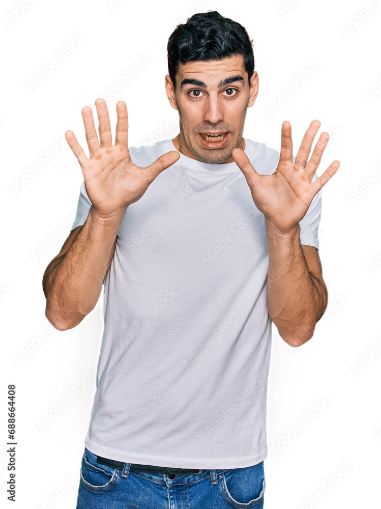 Naklejka premium Handsome hispanic man wearing casual white t shirt afraid and terrified with fear expression stop gesture with hands, shouting in shock. panic concept.