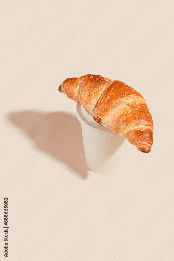 Fresh delicious croissants with an eco cup on a light background.