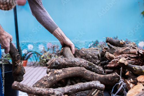 Photo of the hands of an elderly man stacking firewood in the garden of his house for the winter.