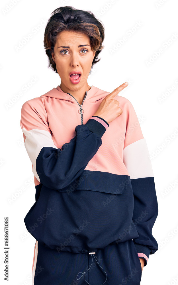 Young beautiful woman wearing sportswear surprised pointing with finger to the side, open mouth amazed expression. Young beautiful woman wearing sportswear surprised pointing with finger to the side, open mouth amazed expression.