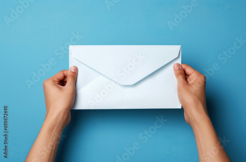 Close-up of hands holding a white envelope against light blue background photo
