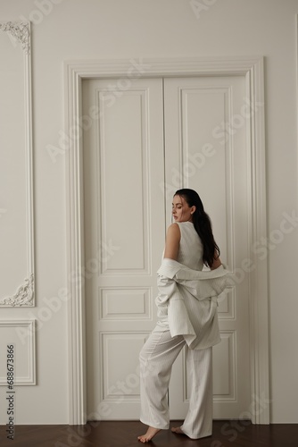 A graceful and stylish young woman, with dark hair and dressed in a white suit, displaying her photogenic qualities within the luminous ambiance of a studio.