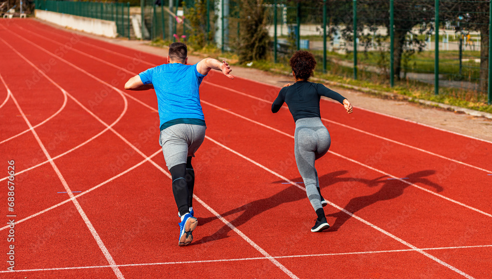 Rear view of woman and man doing morning workout outdoors running on track.
